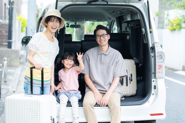 家族で旅行へ。ミニバンの荷室に座る家族とスーツケース