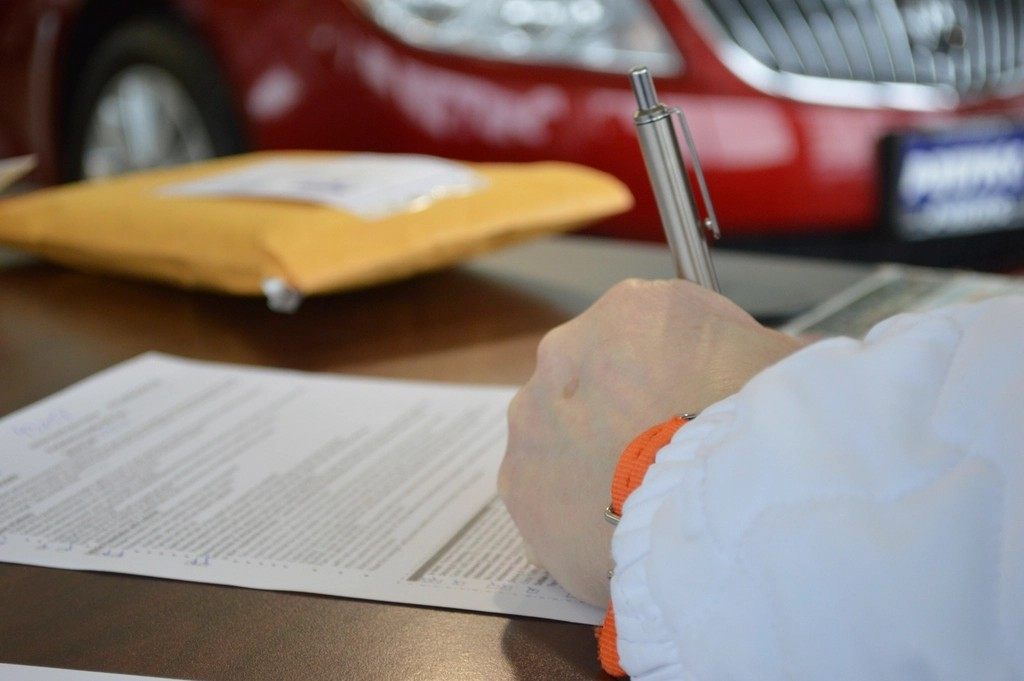 車の前で書類に記入する手元